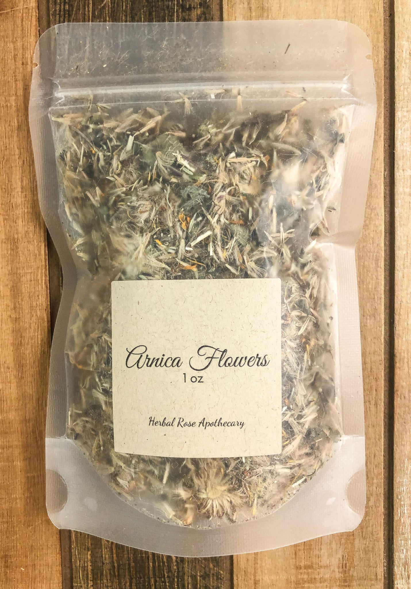 dried arnica flowers in a clear plastic bag with a Kraft colored labeled with herb name and size of 1oz with a wooden background