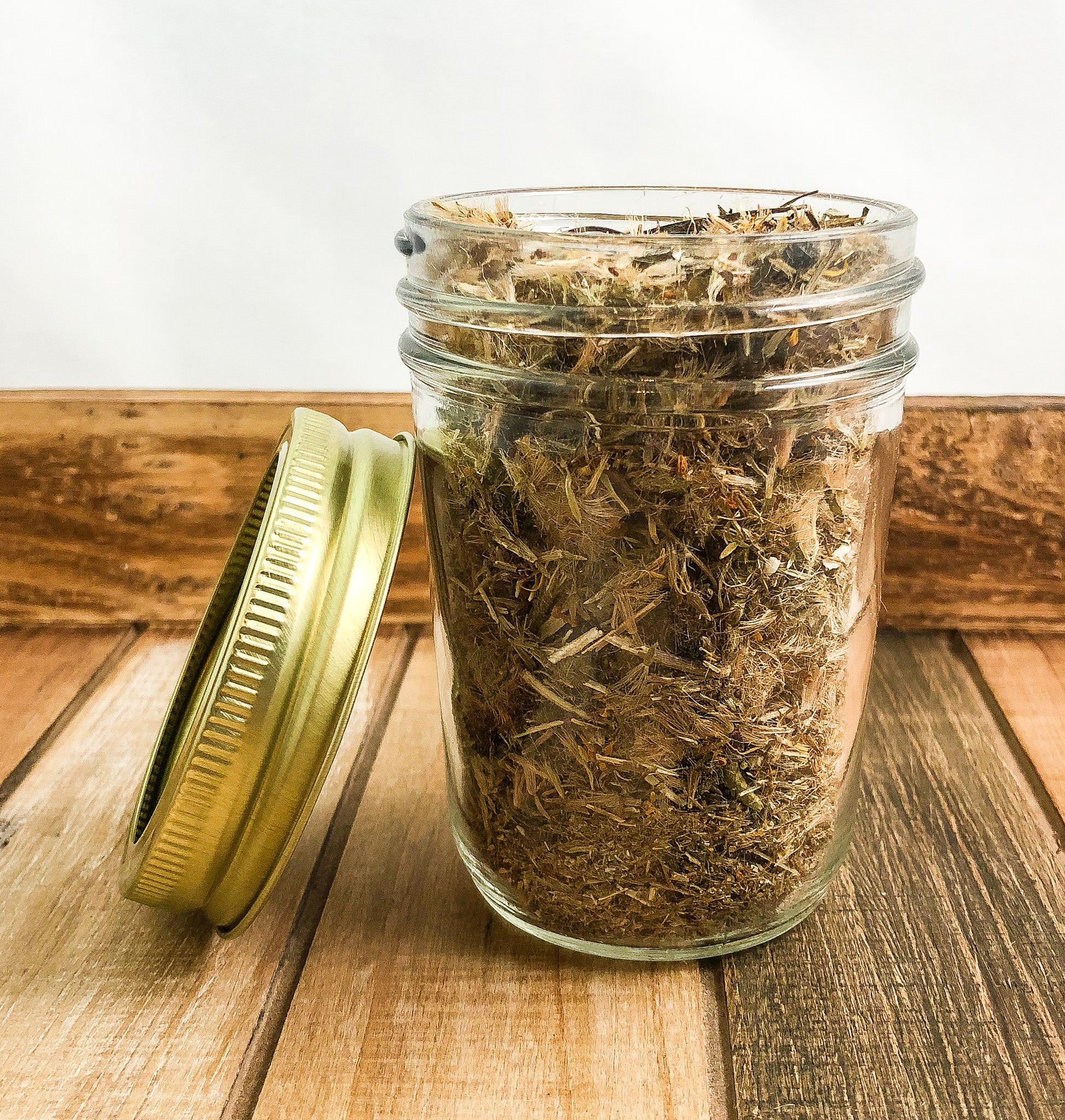 dried arnica flowers in a clear mason jar with a wooden background