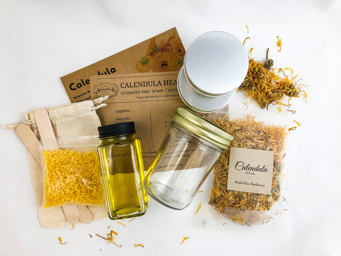 calendula oil and salve making kit on white background. Kit includes calendula monograph, step by step directions, 2 metal tins, dried calendula, mason jar, carrier oil, muslin bag, 2 tongue depressors, and beeswax
