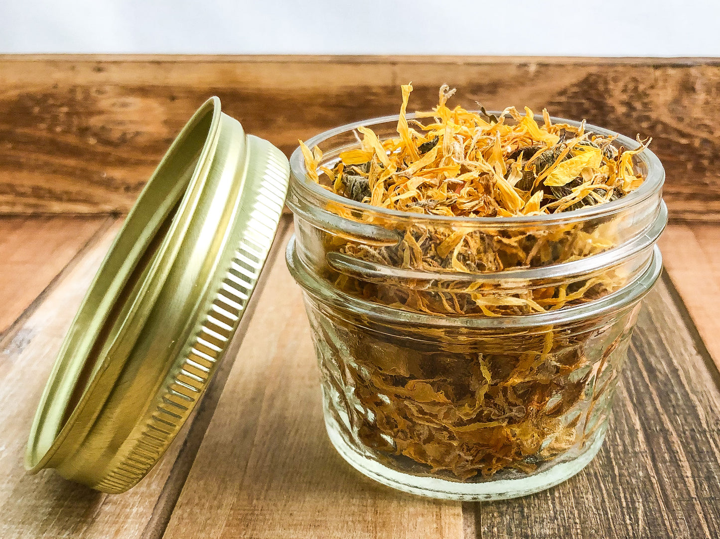dried calendula in a clear mini mason jar with a wooden table and a white background