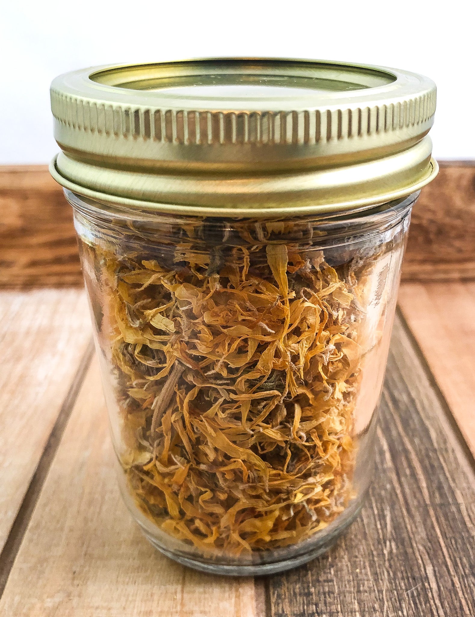 dried calendula in a clear mason jar with a wooden background