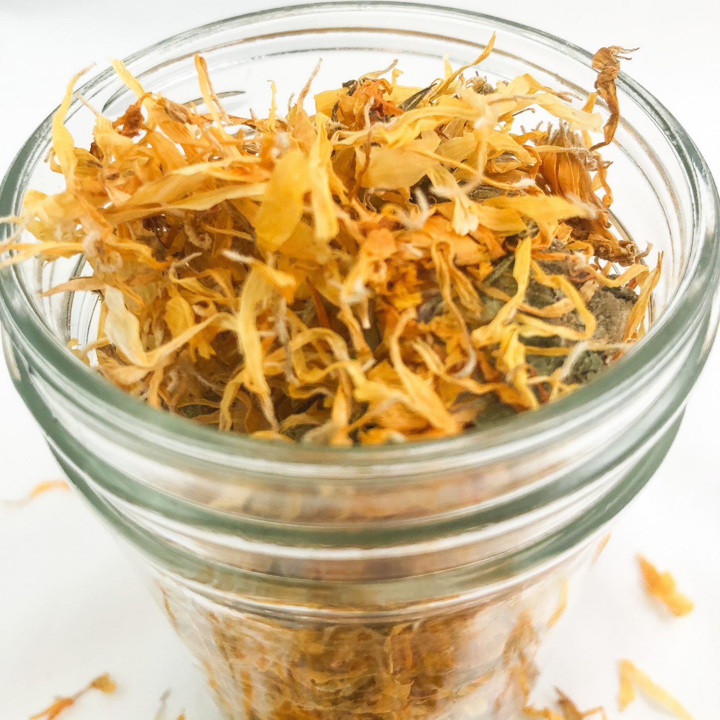 upclose image of dried calendula flowers in a clear glass jar with white background