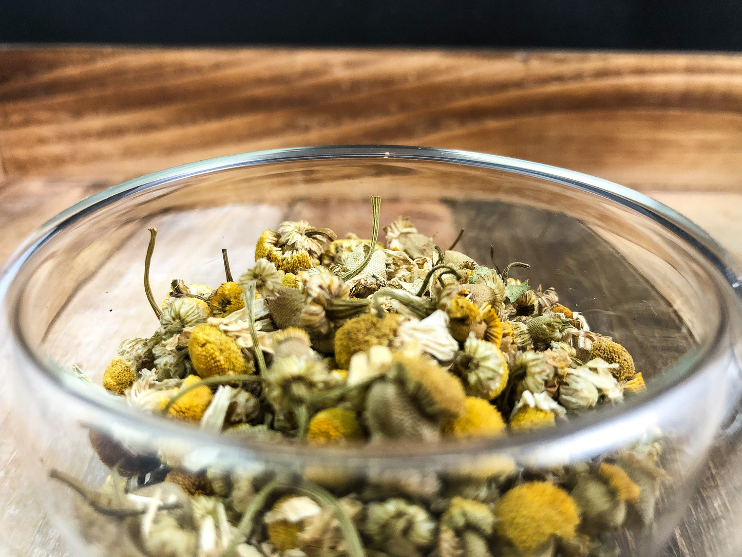 dried chamomile upclose in clear glass cup with wood background