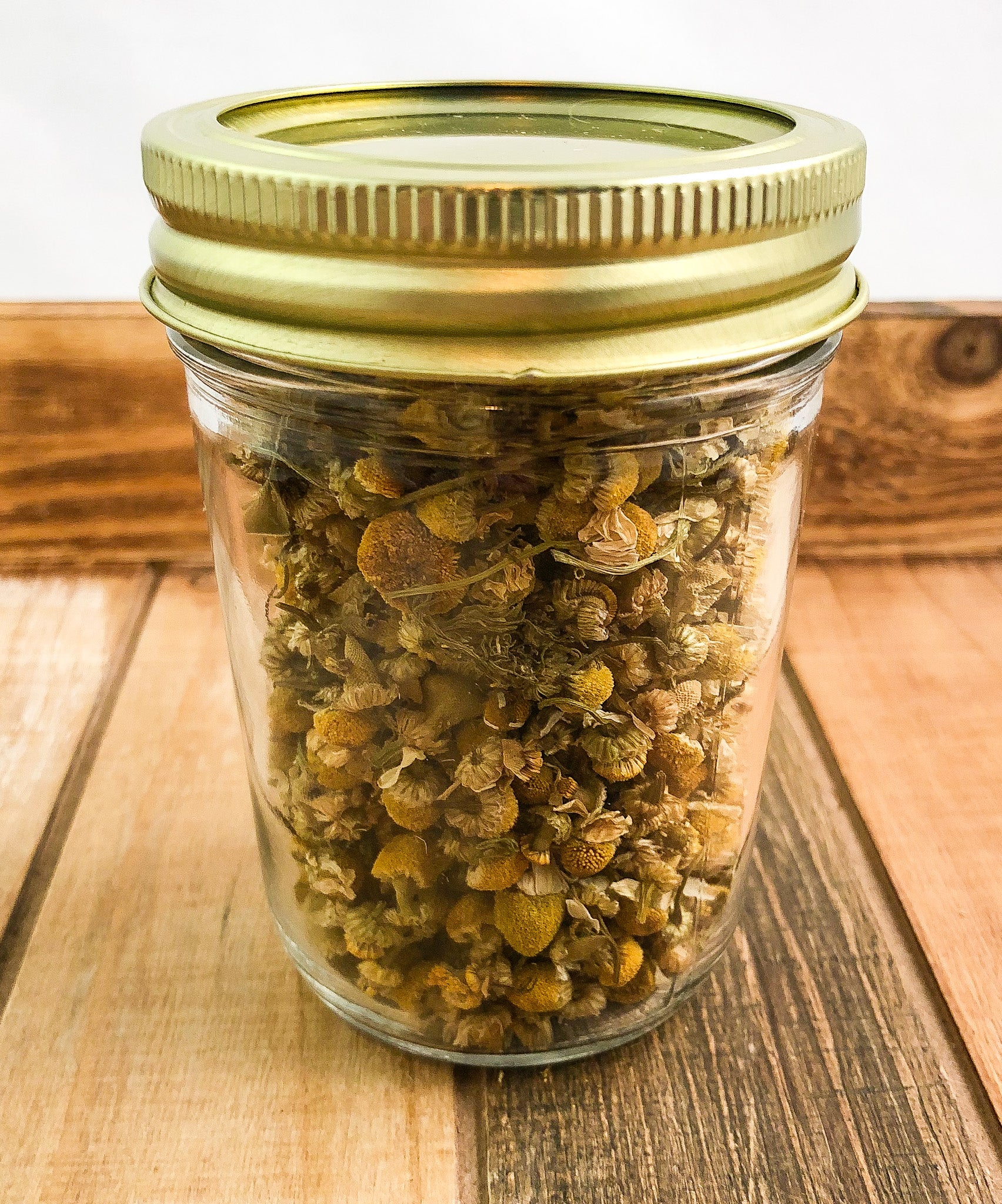 dried chamomile in a clear mason jar with a wooden background