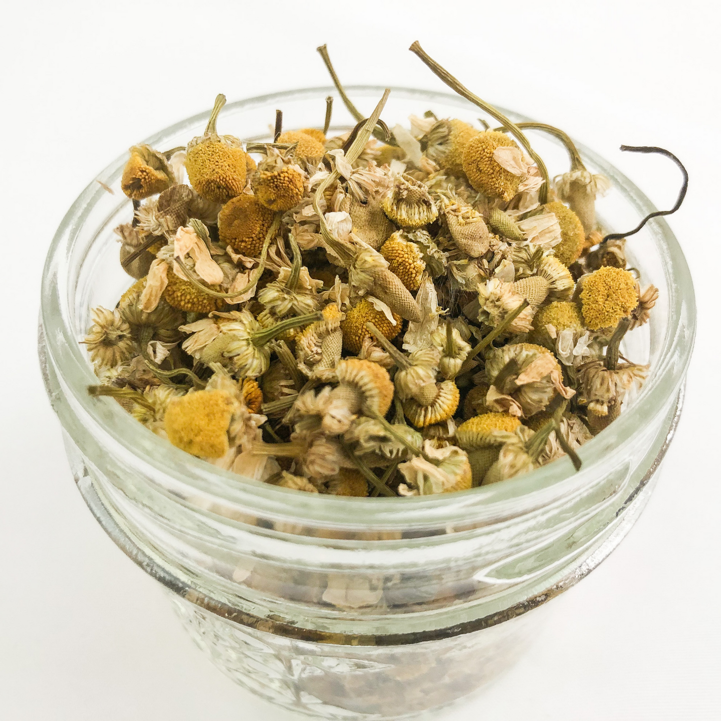 upclose image of dried chamomile in a clear glass jar with white background