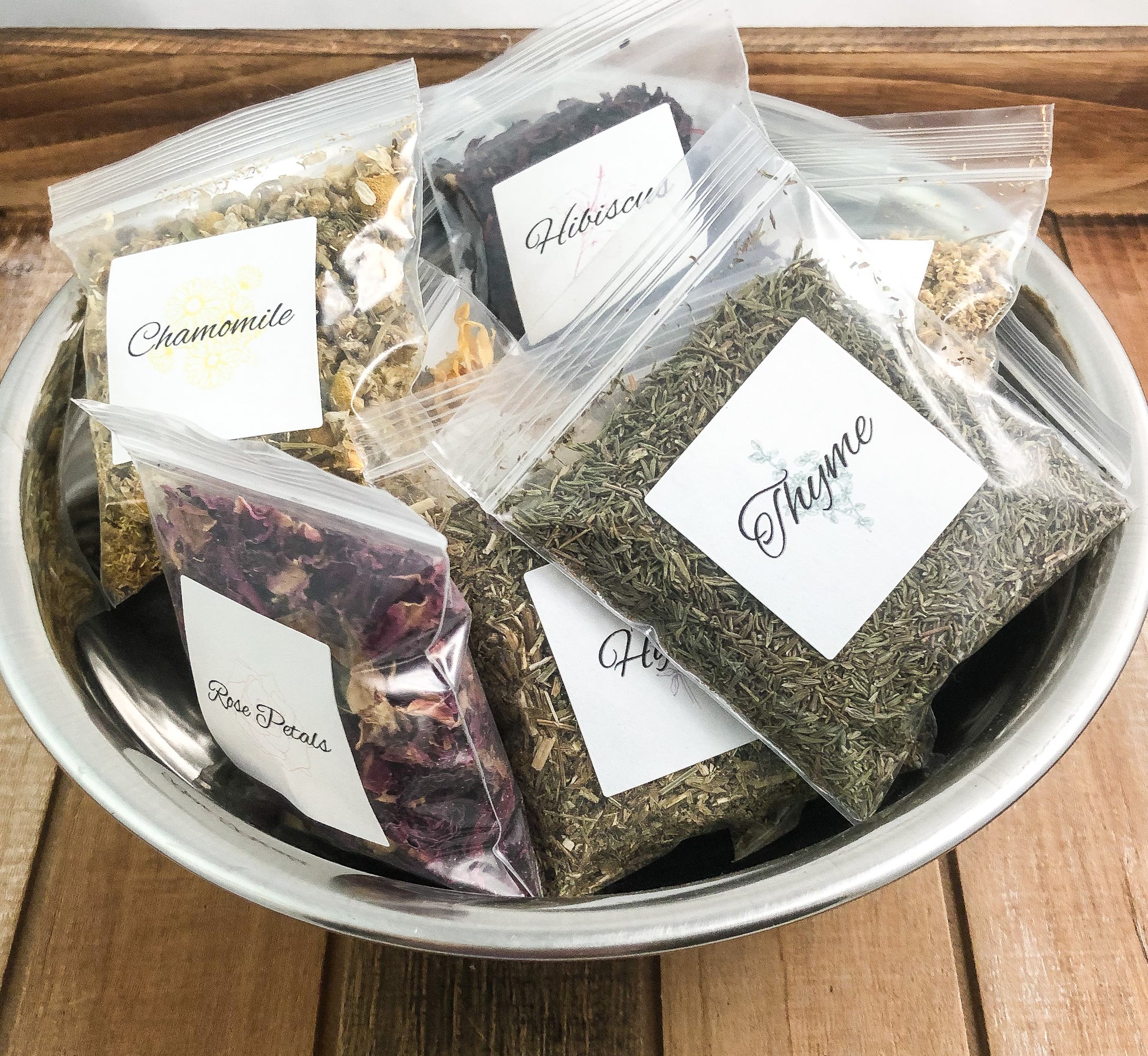 dried herbs in sample bags 8g bags in a silver bowl on a wooden table with white background