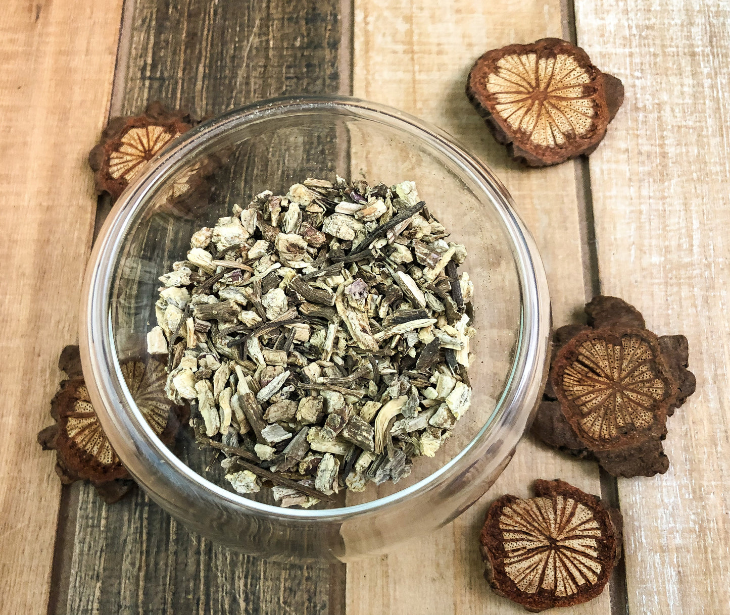 Ariel view of dried echinacea in a small clear glass cup with three little wooden chips surrounding the cup with a wooden table as background