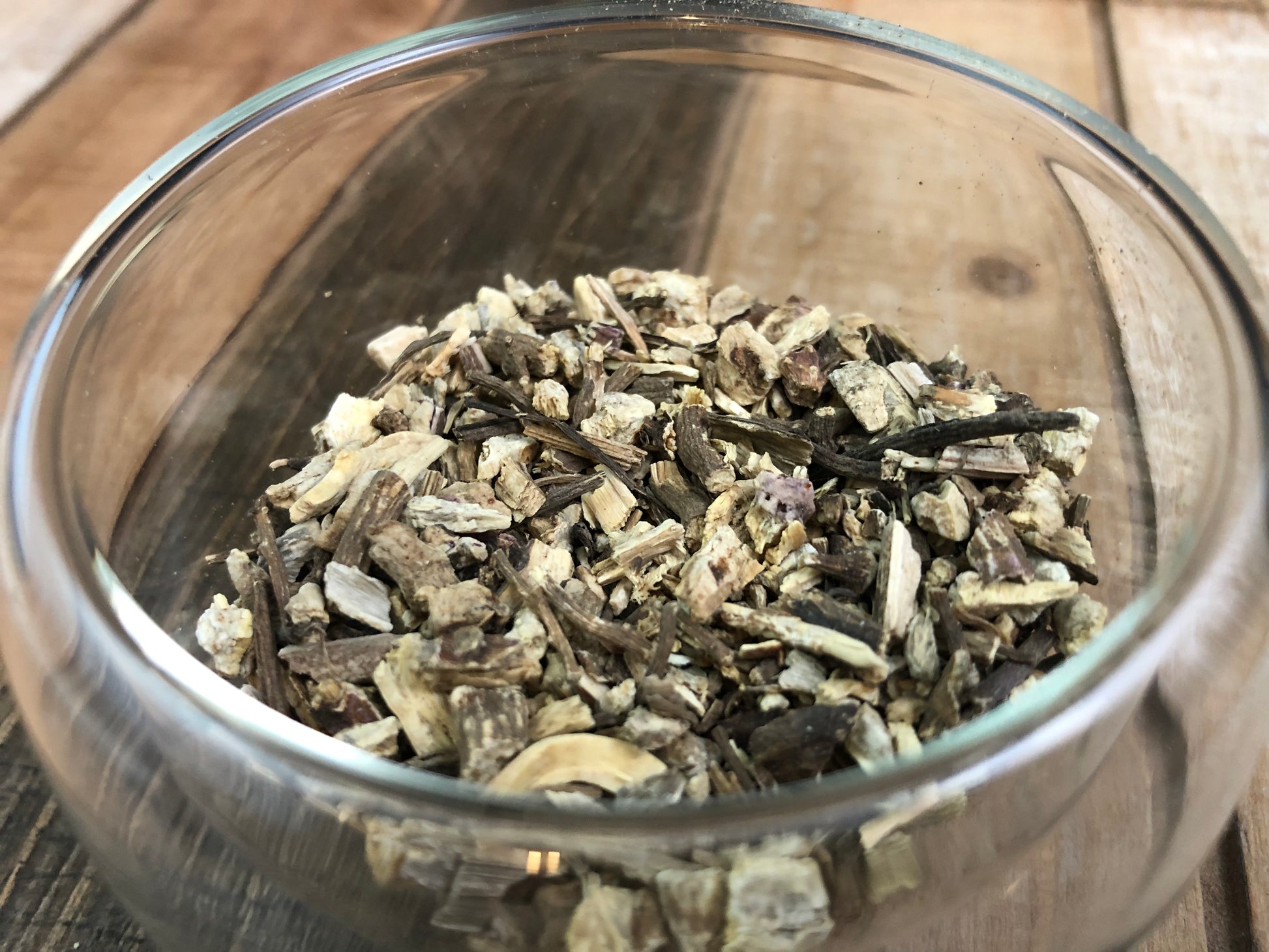 upclose image of dried echinacea in a clear glass cup with a wooden table as background