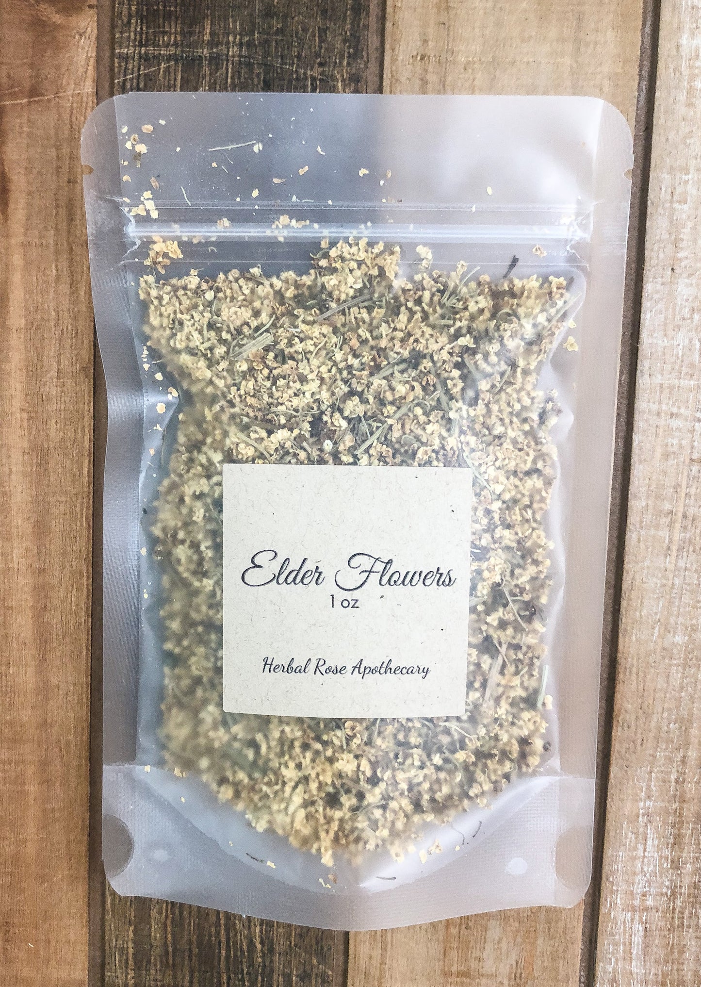 dried elderflowers in a clear bag with brown Kraft label reading elderflowers 1oz with a wooden background