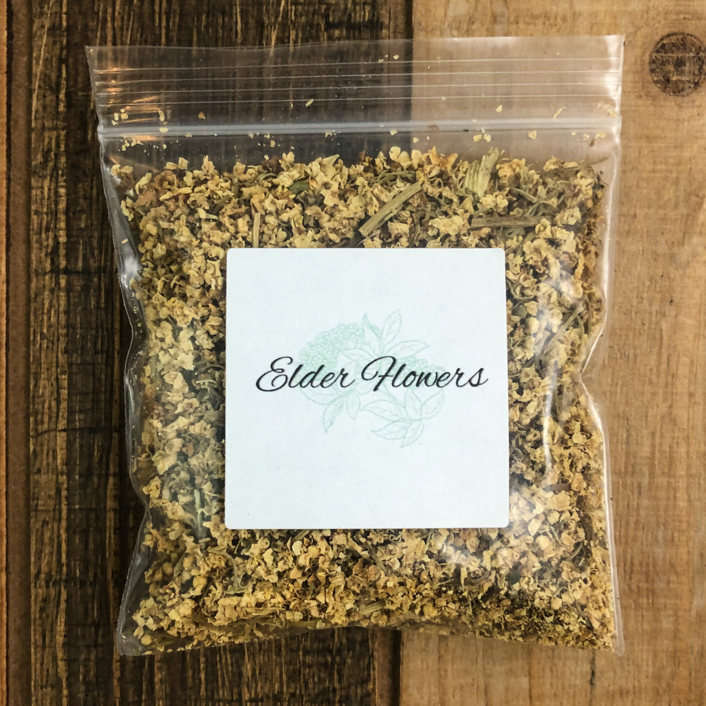 small clear bag of dried elderflowers with a wooden background