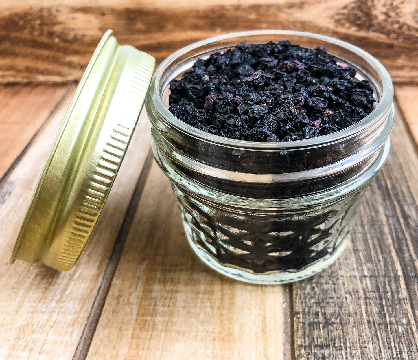 dried elderberry in a clear mini mason jar with a wooden background