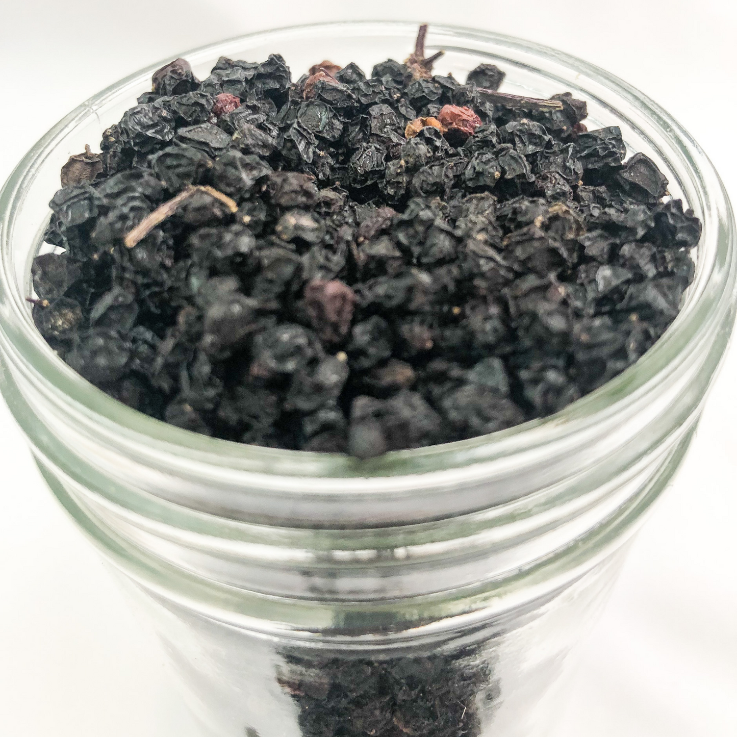 upclose image of dried elderberries in a clear glass jar with white background