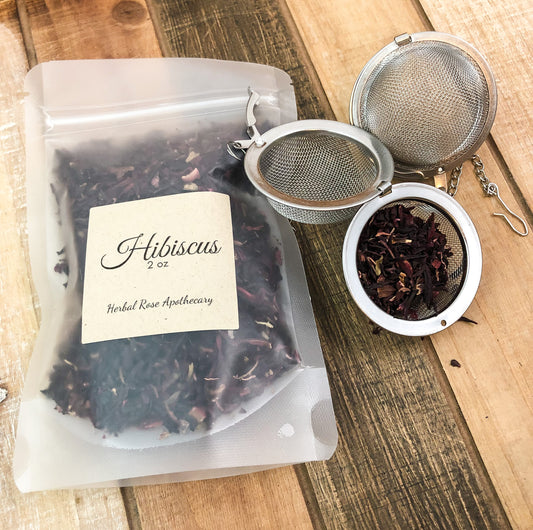 dried hibiscus in a clear 1oz bag next to a mesh tea infuser with dried hibiscus, items on a wooden table as background