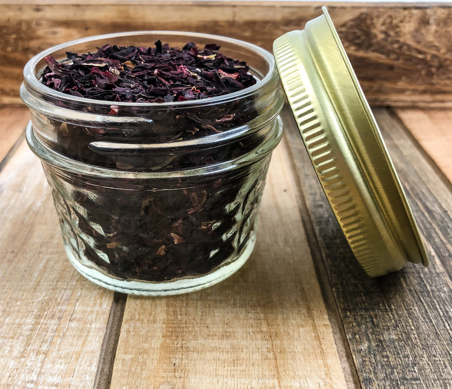 dried hibiscus in a clear mini mason jar with a wooden background