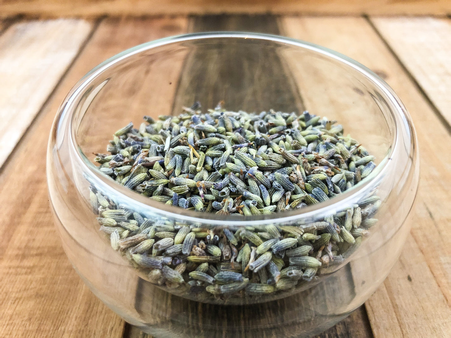 upclose image of dried lavender in a clear glass cup on a wooden table as background
