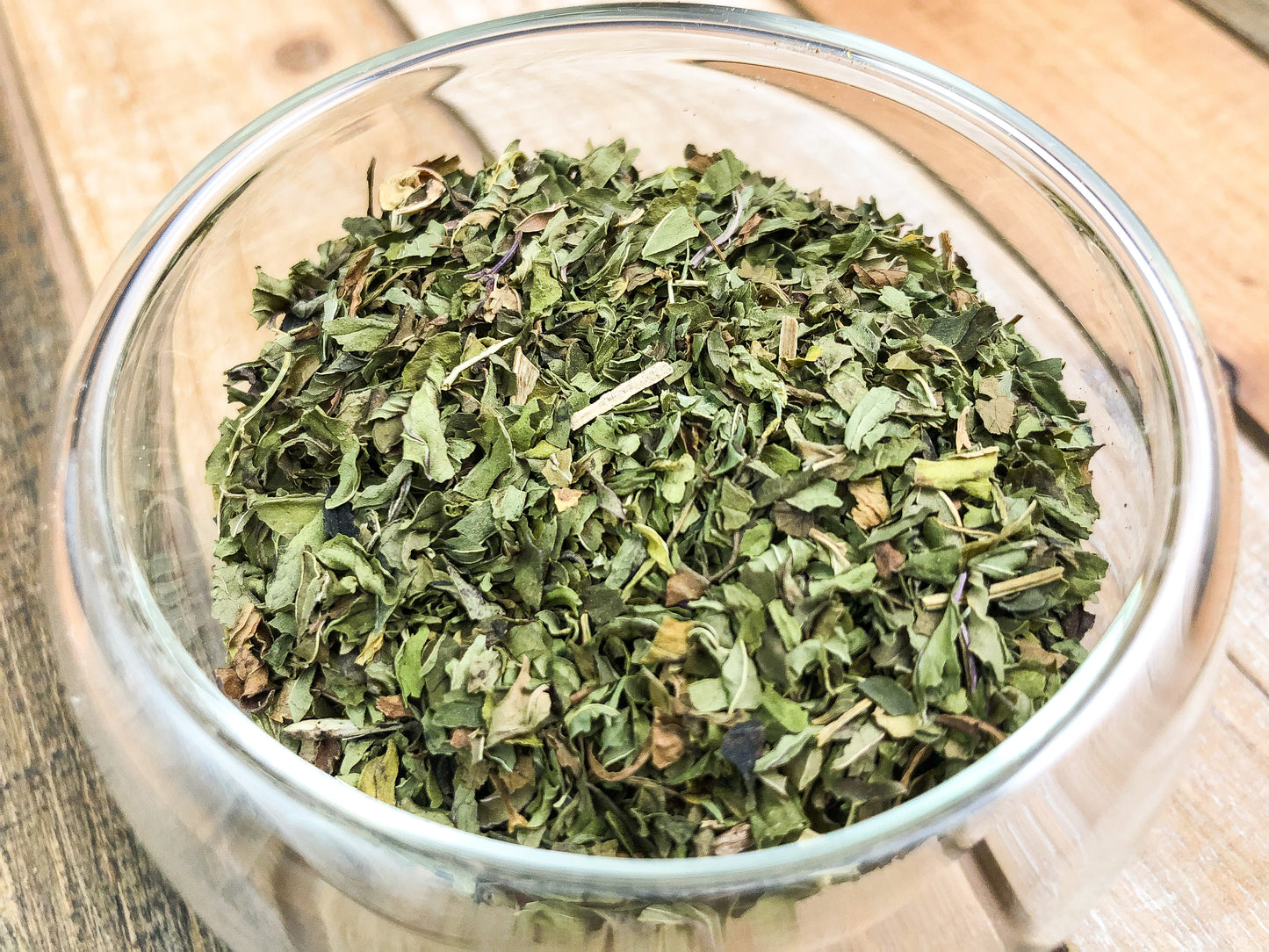 upclose image of dried peppermint in a clear glass cup with a wooden table background