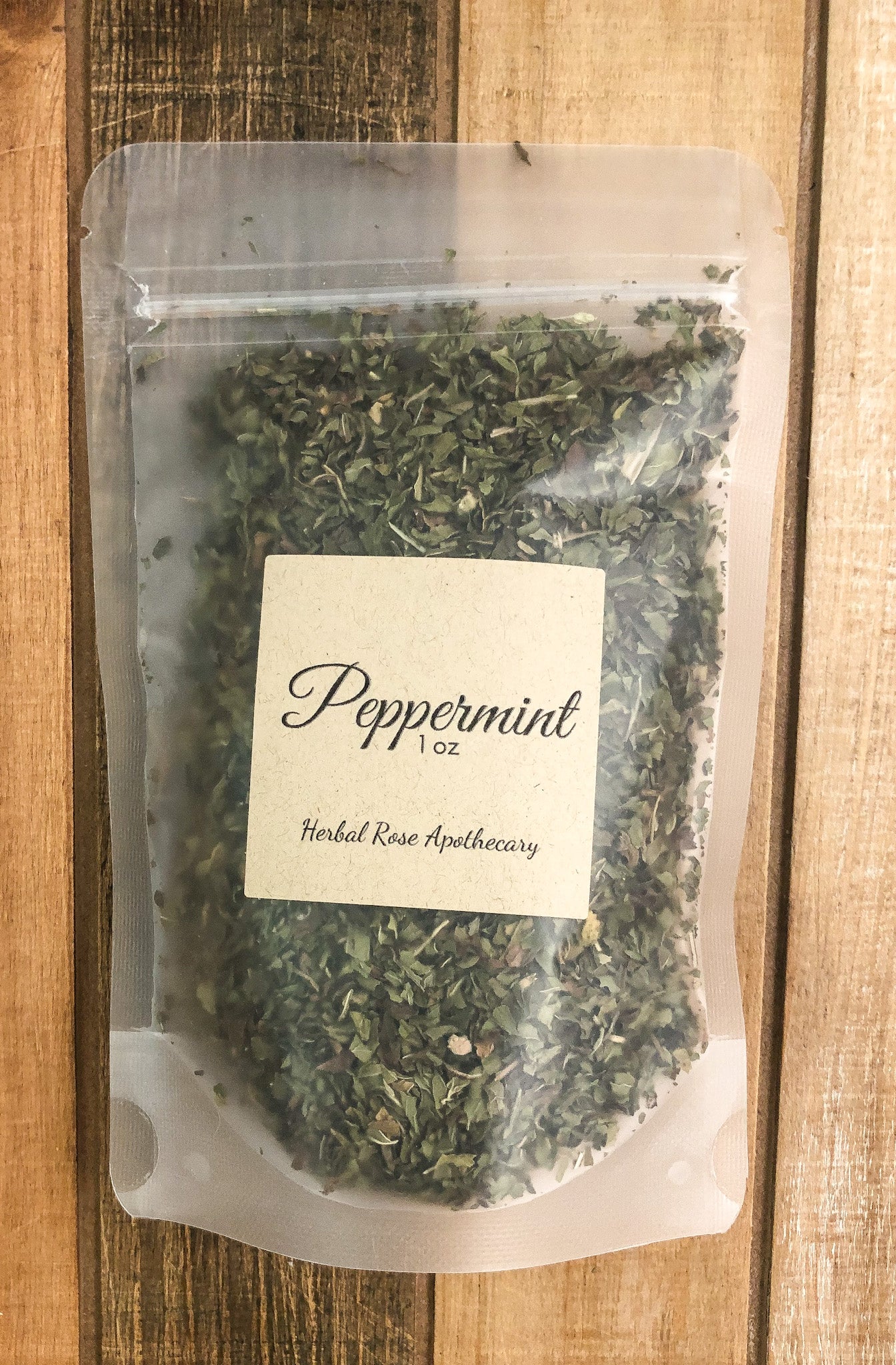 1oz bag of dried peppermint in a clear plastic bag with a wooden background
