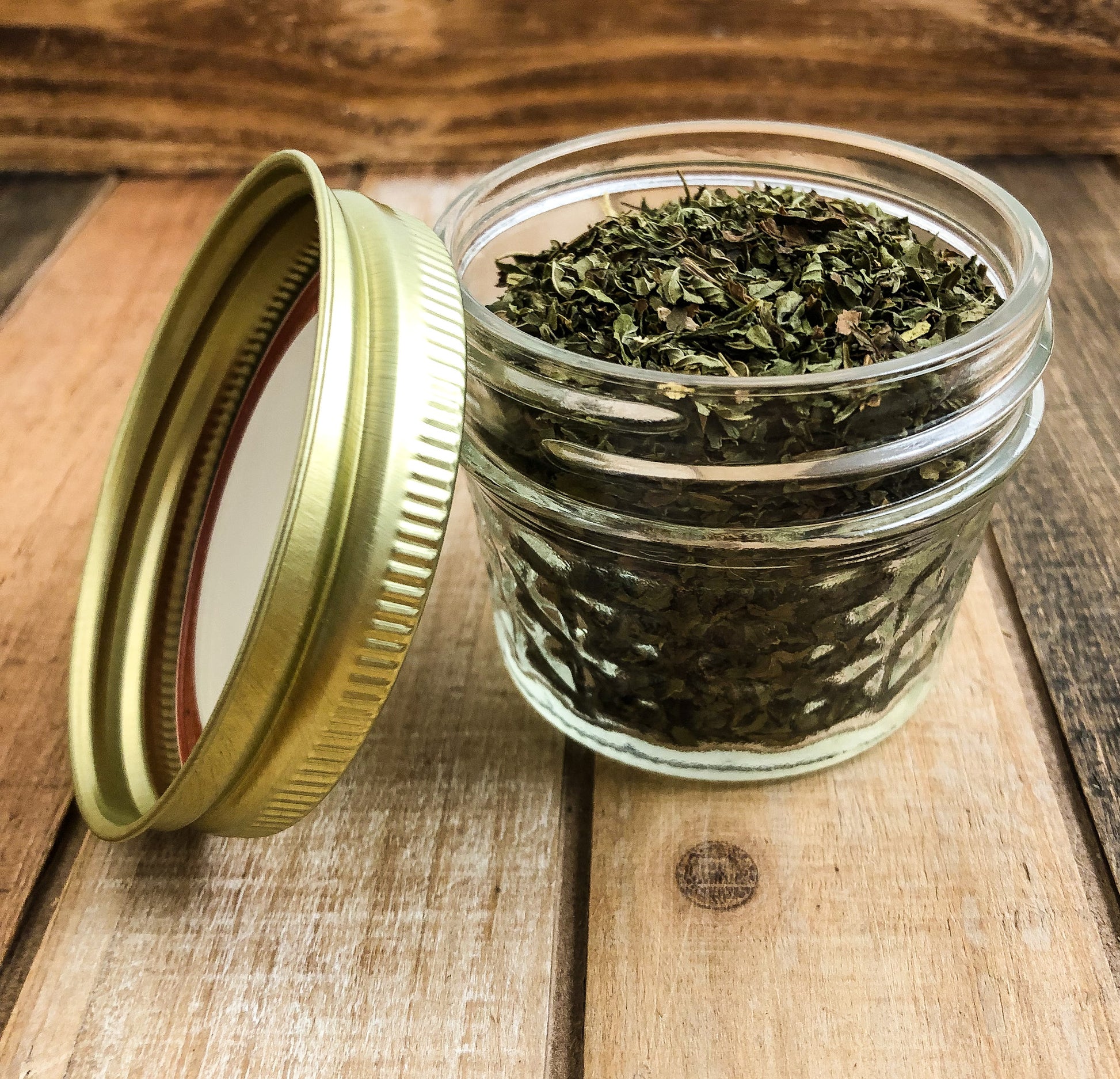 dried peppermint in a clear mini mason jar with a wooden background