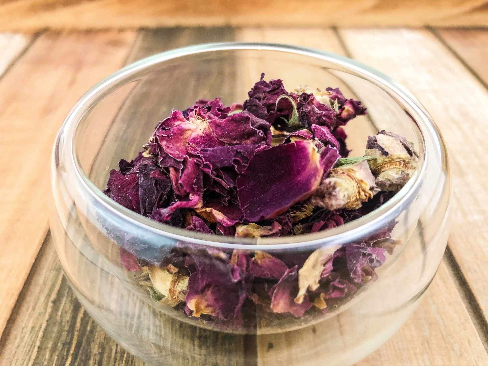 upclose image of dried roses in a small clear glass cup on a wooden table top as background