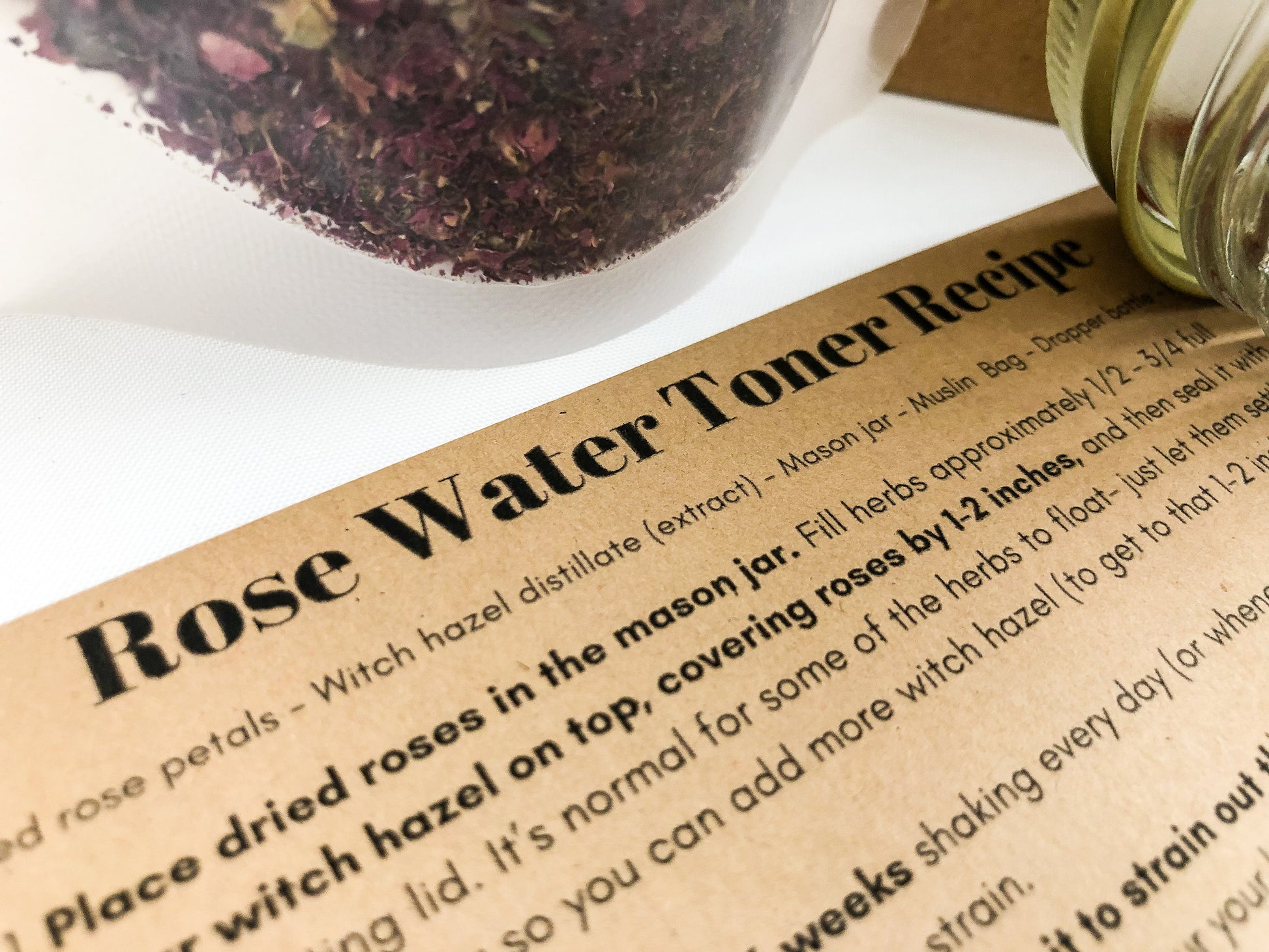 rose water toner recipe, image of recipe upclose at an angle with dried roses in a bag in upper part of image