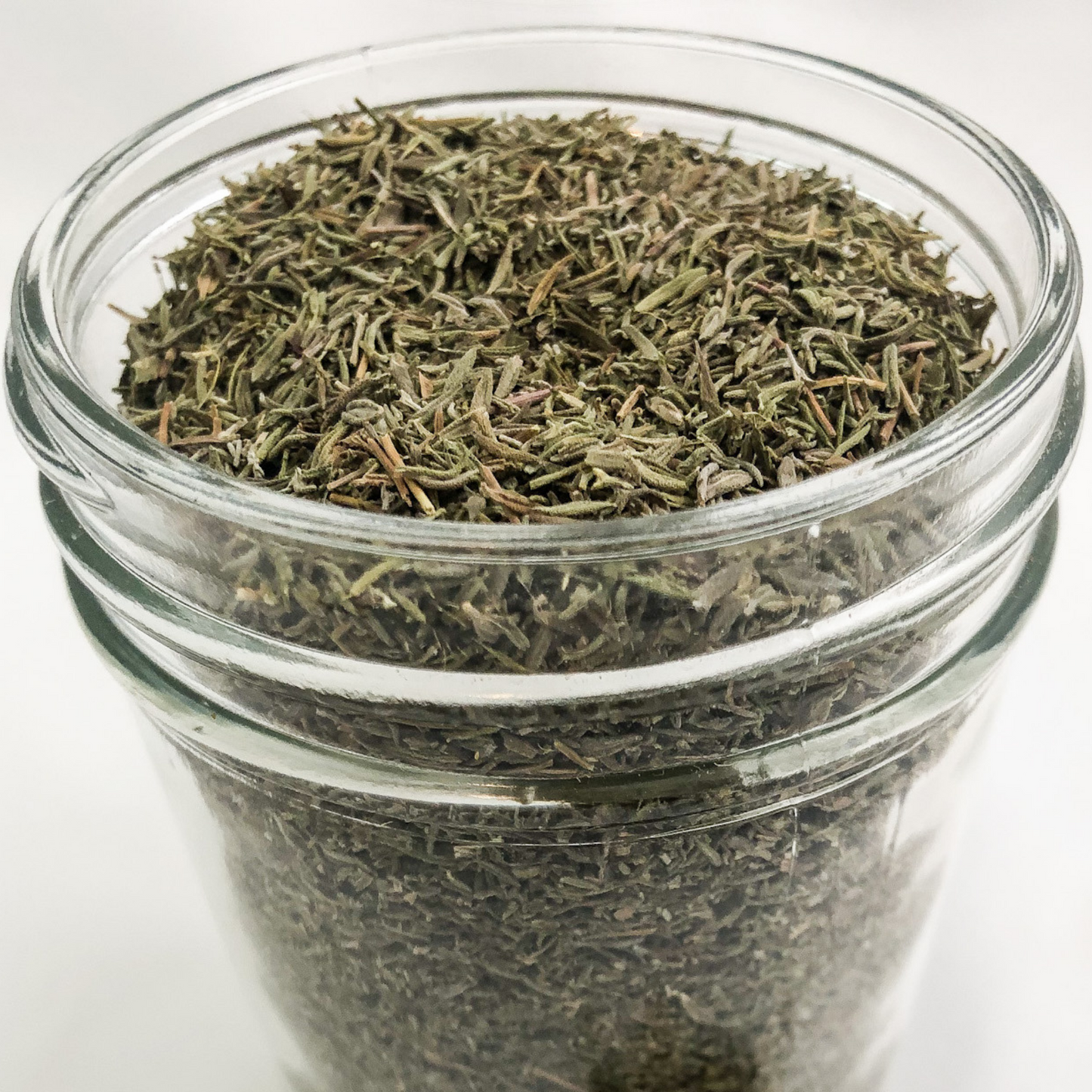 upclose image of dried thyme in a clear glass jar with white background